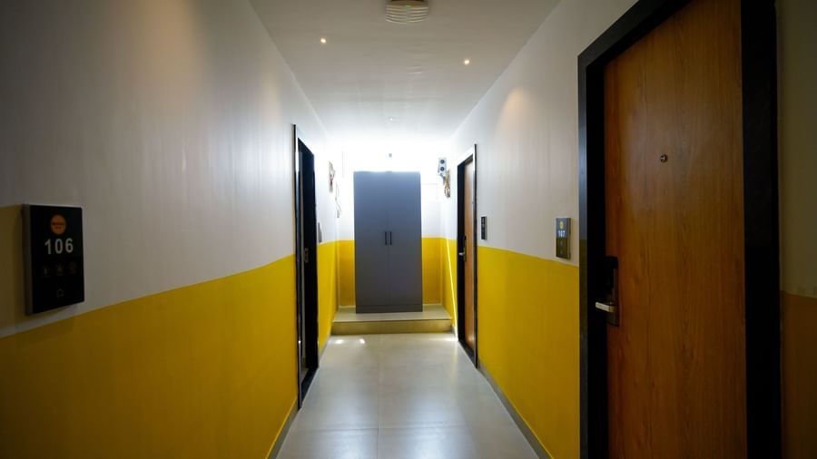 A long, narrow hotel hallway with yellow and white walls, brown doors on either side, and a brightly lit area at the far end - Beestay Hotels Financial District, Hyderabad 
