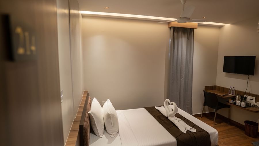 Double bed with curtains, wall-mounted TV, and cosy atmosphere at Beestay Hotels, Rajahmundry.