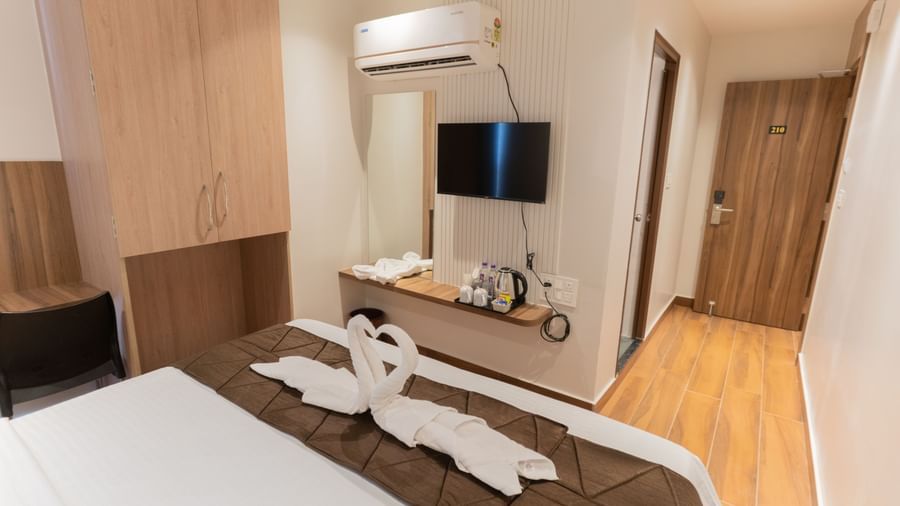Neatly designed bedroom with wall-mounted TV and seating area beside the bed at Beestay Hotels, Rajahmundry.