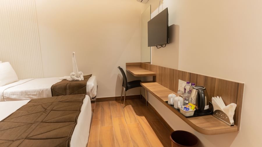 Twin beds with bedside table and wall-mounted TV for convenience at Beestay Hotels, Rajahmundry.