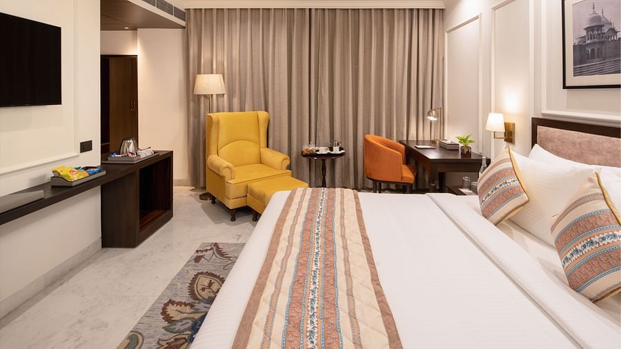 An image of a bedroom with bedside table, photo frame hanged on the wall, work desk with sofa chair, and a flat TV screen - Brij Eternity, Vrindavan