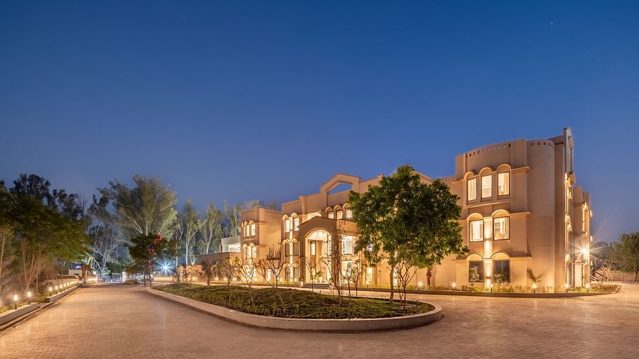 An image of a well lit facade with a huge concrete lawn and a few trees - Brij Eternity, Vrindavan