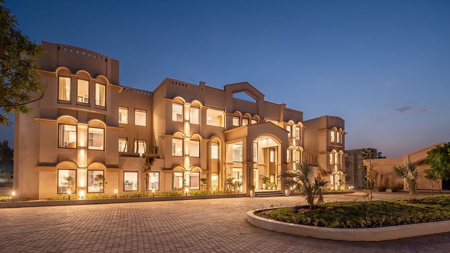 An image of a well lit facade with a huge concrete lawn and a few trees - Brij Eternity, Vrindavan