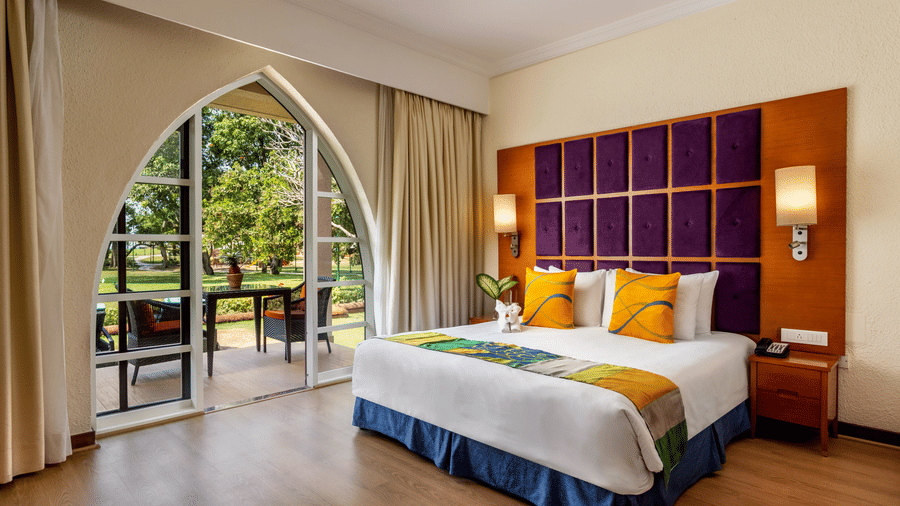 a king bed with cushioned headboard, lamps and side tables inside 2 Bedroom Garden Villa - Caravela Beach Resort Goa