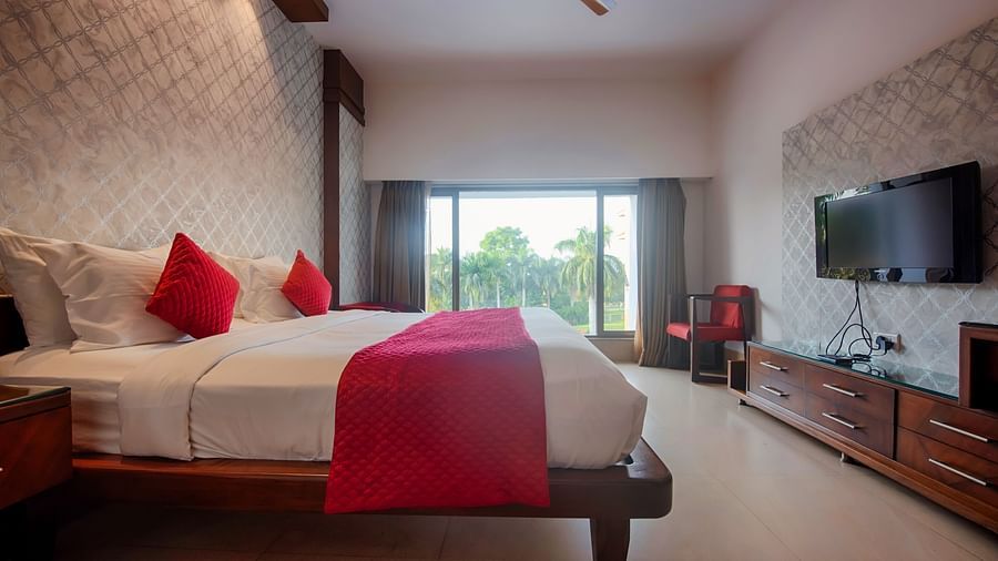 Club Room at Crescent Resort, Sehore showcasing a plush bed with cushions and bed runner facing a TV mounted on the wall under warm lighting and subtle daylight coming through a large window
