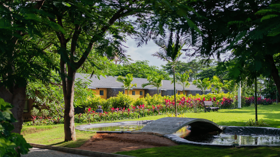 Premium room villas with a small pond and lawn in the foreground at Darza Resorts near Maruthamalai Murugan Temple, with clear blue sky in the background.