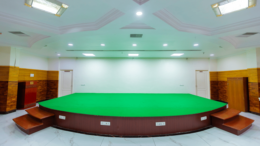 The stage at Irudhayam Hall, DSF Grand Plaza, Tuticorin with a green carpeted platform, wooden side steps, and doors flanking a plain backdrop wall.