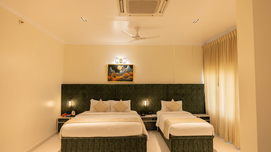 Guest room at DSF Grand Plaza, Tuticorin with a double bed and single bed, green headboards, matching nightstands, ceiling fan, and an air conditioner.