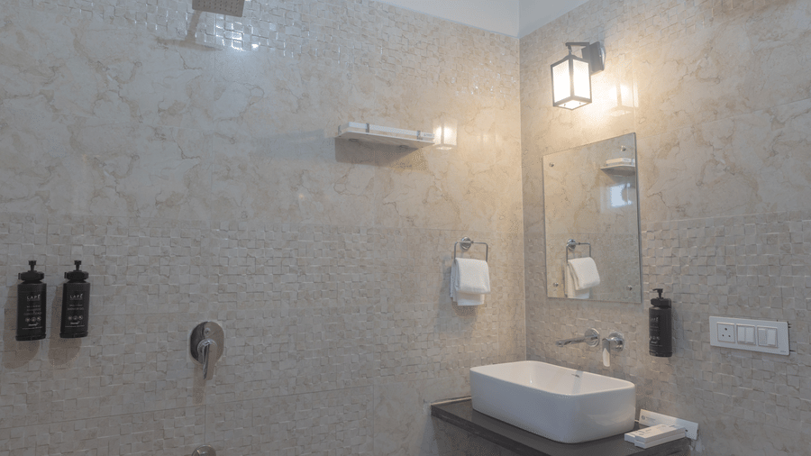 A bathroom at Estherea Bagh, Ranthambore, showing a vessel sink on a dark counter, a mirror, and textured light-coloured walls.