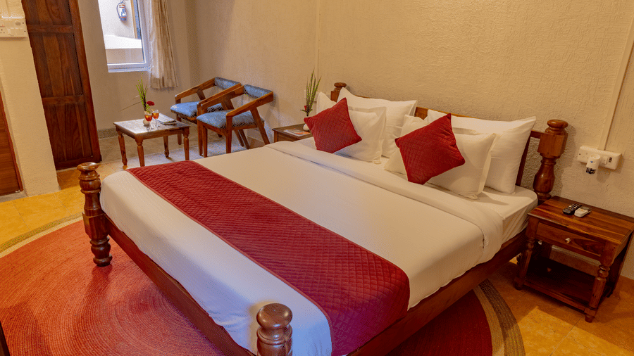 A bedroom view at Estherea Bagh, Ranthambore, showing a bed with red and white bedding and a small bedside table.
