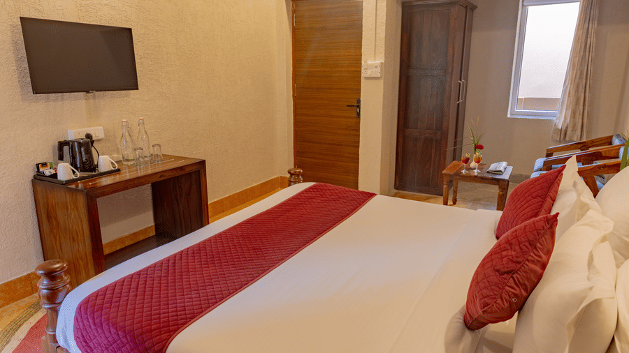 A guest room at Estherea Bagh, Ranthambore, with a double bed, a wall-mounted TV, and a wooden desk.