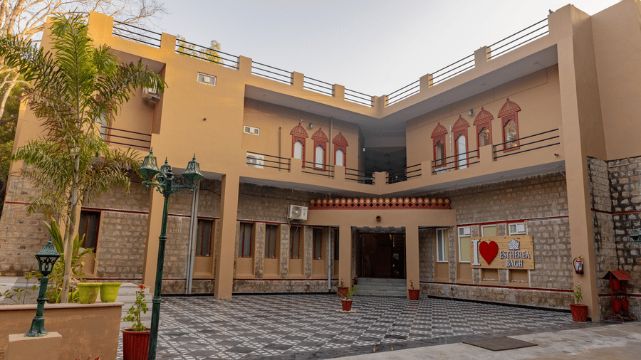 Exterior of the multi-storey tan main building at Estherea Bagh, Ranthambore, with trees and a paved courtyard.