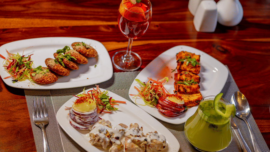 Several appetizer plates and colorful drinks arranged on a dark wood dining table at Estherea Bagh, Ranthambore.