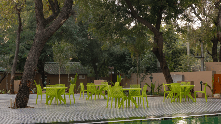 Outdoor seating area at Estherea Bagh, Ranthambore, with several green chairs and tables arranged near a swimming pool.