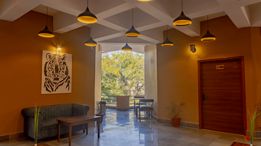 Common area at Estherea Bagh, Ranthambore, with seating, tiger artwork, and an open doorway leading to an outdoor balcony.