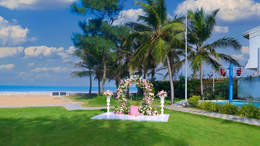 An outdoor decorated space with green trees at the back and the sea & partly clouded sky visible at the backdrop at Grande Bay Resort & Spa.