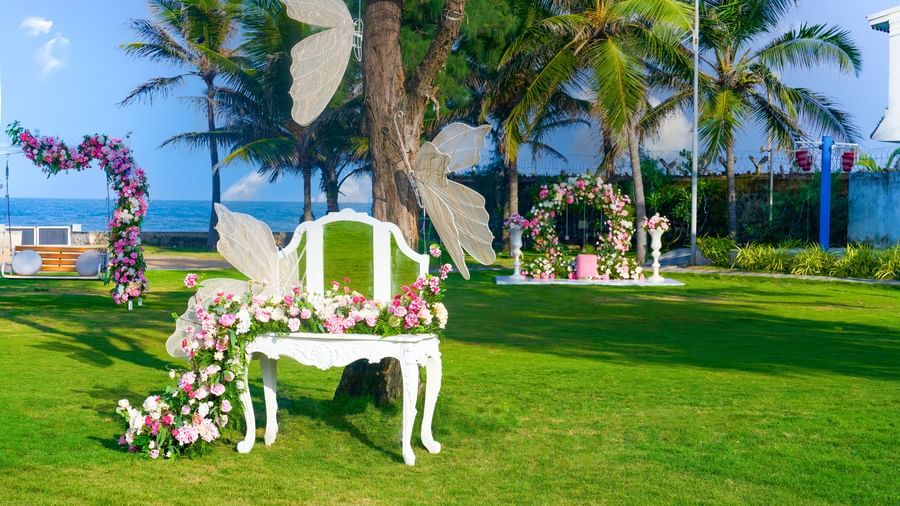 A flowery decorated chair in an outdoor lawn with artificial butterflies attached to the chair and the tree with greenery at the backdrop at Grande Bay Resort & Spa.