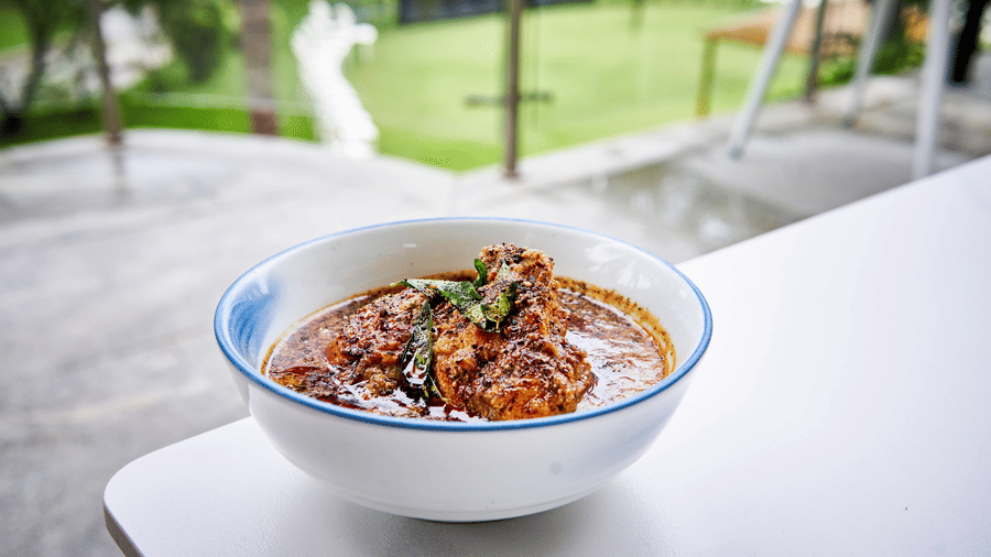 Bowl of rich curry placed on a white table with a lawn and coconut trees in the background - Grande Bay Resort & Spa, Mamallapuram