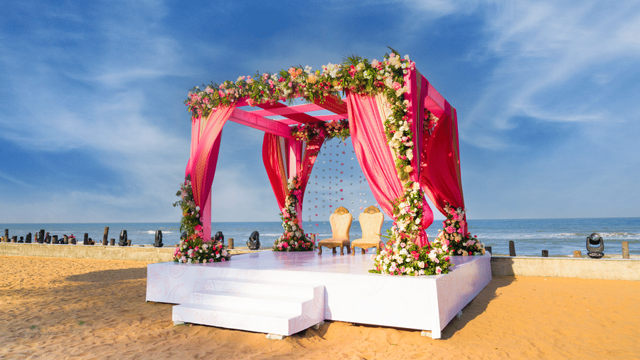 Pink floral mandap setup on the beach with draped fabric and white platform - Grande Bay Resort & Spa, Mamallapuram