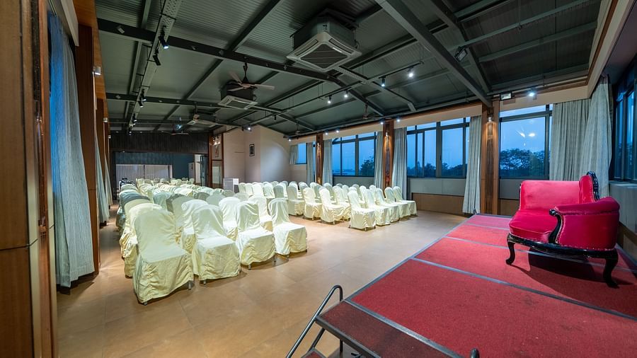 A view from near the stage at Hari Govinda's Express, Vijayanagar, reveals a central aisle with rows of chairs on either side, leading to a stage with a cushioned sofa.