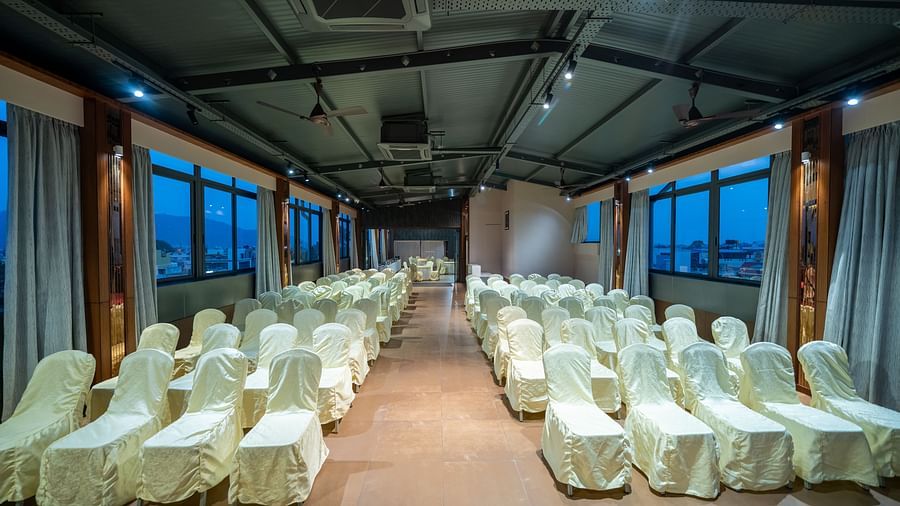 A front view of the banquet hall at Hari Govinda's Express, Vijayanagar, shows chairs arranged on both sides of a central aisle, with curtains pulled to the sides of the windows.