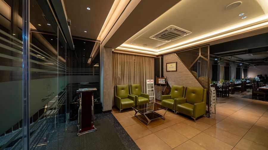 Lobby area at Hari Govinda's Express, Vijayanagar, features L-shaped cushioned sofas with a glass table in front, complemented by warm and welcoming lighting.
