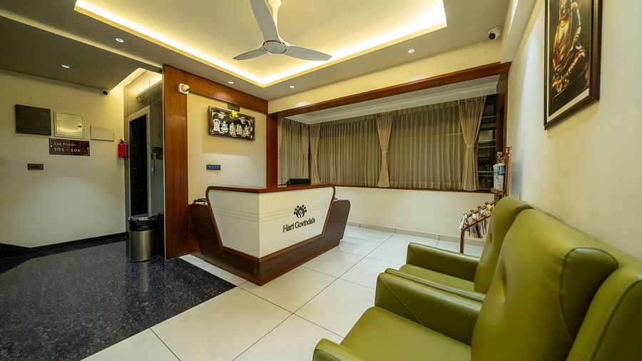 Reception area at Hari Govinda's Express, Vijayanagar, features a desk at one end, cushioned sofas directly opposite, and a photo frame above them.