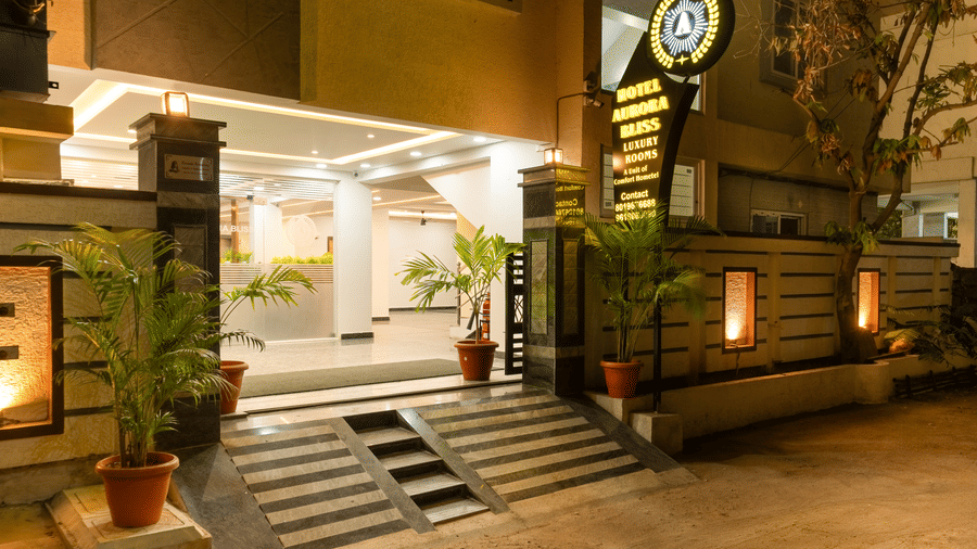 An illuminated entrance of  Hotel Aurora Bliss, Gachibowli, featuring staircase, plants, and the hotel logo.