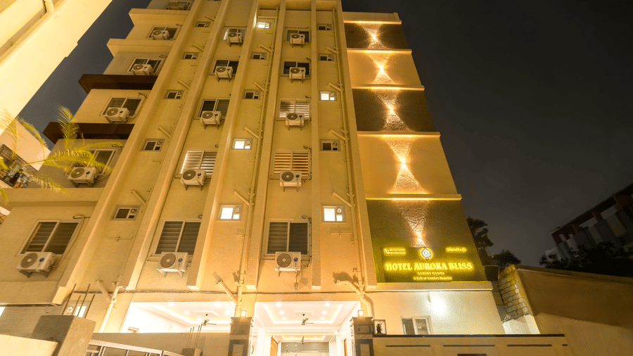 The illuminated facade of Hotel Aurora Bliss, Gachibowli, with several trees around it.