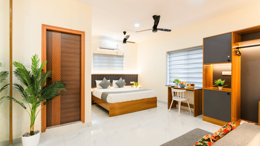 A room at Hotel Aurora Bliss, Gachibowli, featuring a large bed, spreads, pillows, fans, a chair, and a table.