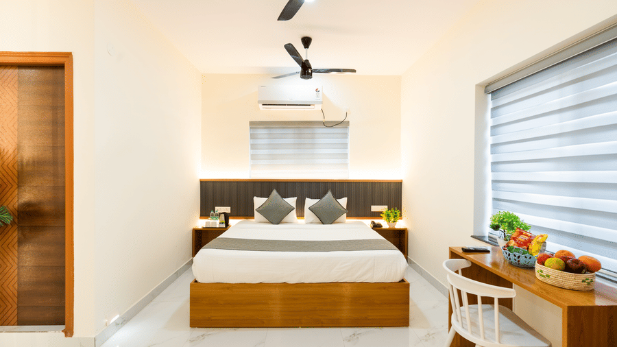 A room at Hotel Aurora Bliss, Gachibowli, featuring a large bed, spreads, pillows, fans, a chair, and a table.