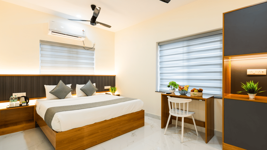 A room at Hotel Aurora Bliss, Gachibowli, featuring a large bed, spreads, pillows, fans, a chair, and kitchenette.