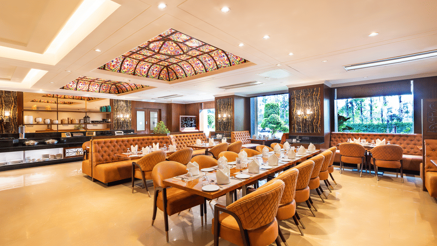 Long view of the spacious restaurant with multiple dining tables, comfortable seating, and a view of the outside through windows at Hotel Hukam's Lalit Mahal.