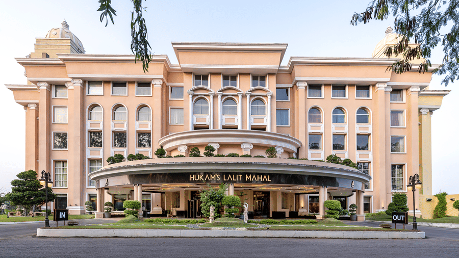 Large, modern, multi-storey building in a peachy-pink colour with a curved canopy entrance and formal landscaping at Hotel Hukam's Lalit Mahal.