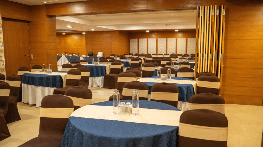 Regency One, one of the best banquet halls in Udaipur, with round tables draped in blue tablecloths and brown chairs, arranged for an event at Hotel Udai Median, Sukhadia Circle.