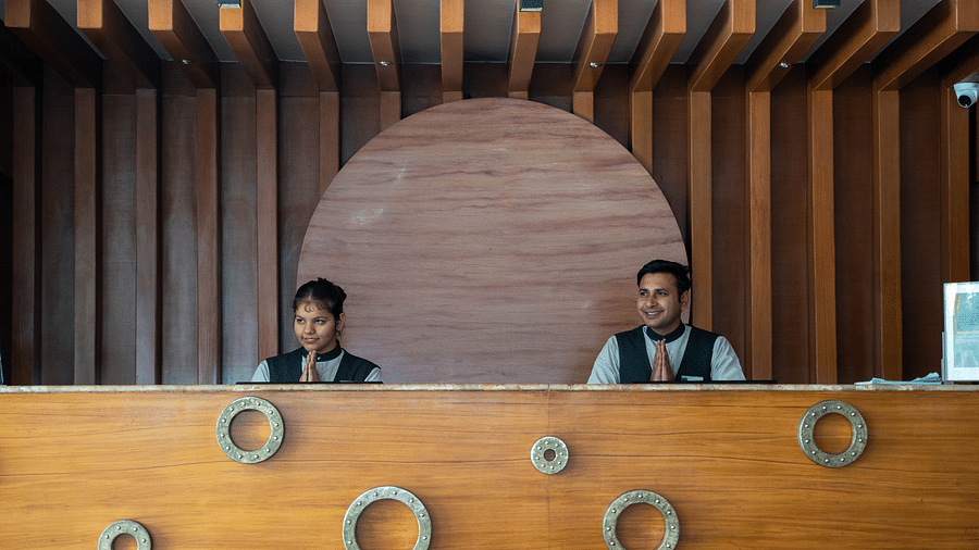 Two hotel staff members standing behind a stylish wooden reception counter with circular design accents - Hotel Udai Median, Udaipur.