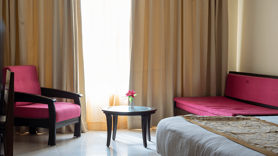 A hotel room with a seating area featuring two armchairs, a coffee table, and large windows with golden curtains - Hotel Udai Median, Udaipur.