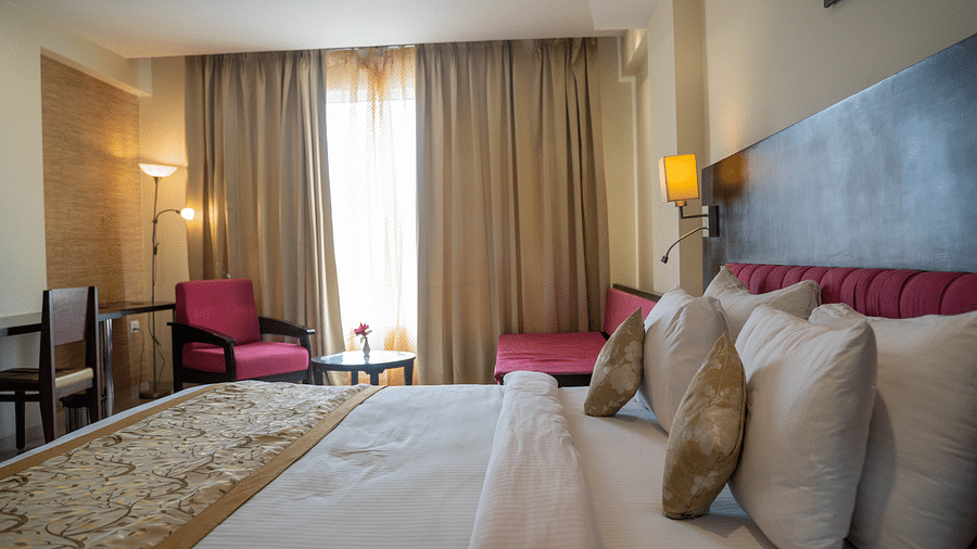 A spacious hotel room with a large bed, armchairs, and floor-to-ceiling curtains - Hotel Udai Median, Udaipur.