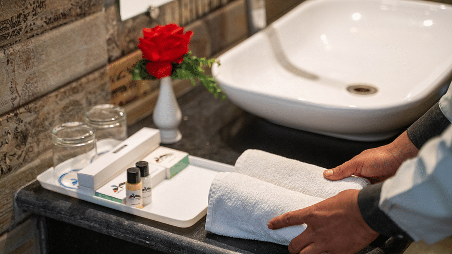 A staff member preparing a bathroom counter with fresh towels, toiletries, and a flower vase - Hotel Udai Median, Udaipur.
