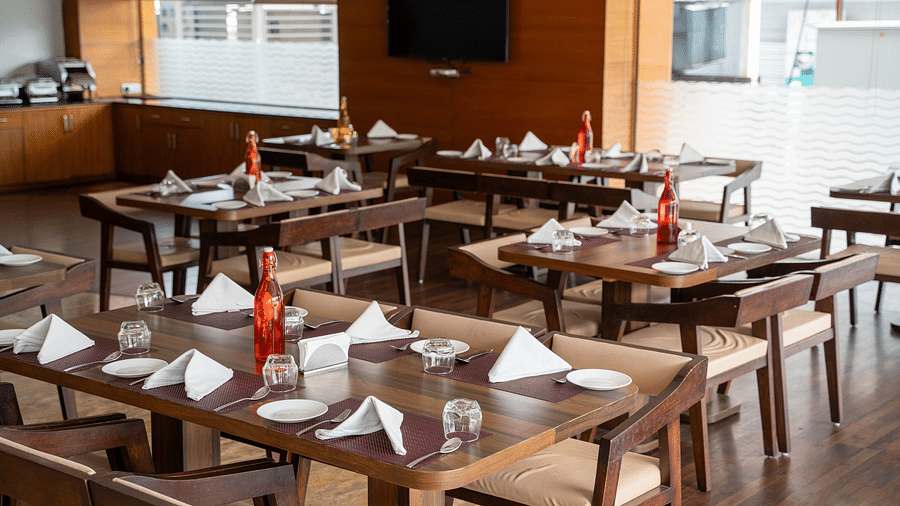 An elegant indoor restaurant setup with polished wooden tables, folded napkins, and large windows providing natural light - Hotel Udai Median, Udaipur.