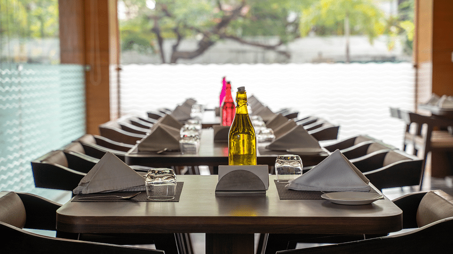 An outdoor dining area with wooden tables, neatly folded napkins, and decorative bottles - Hotel Udai Median, Udaipur.