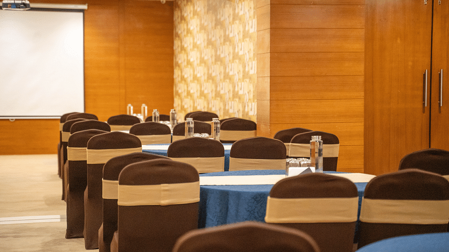 A spacious conference room with rows of round tables, upholstered chairs, and a presentation screen - Hotel Udai Median, Udaipur.