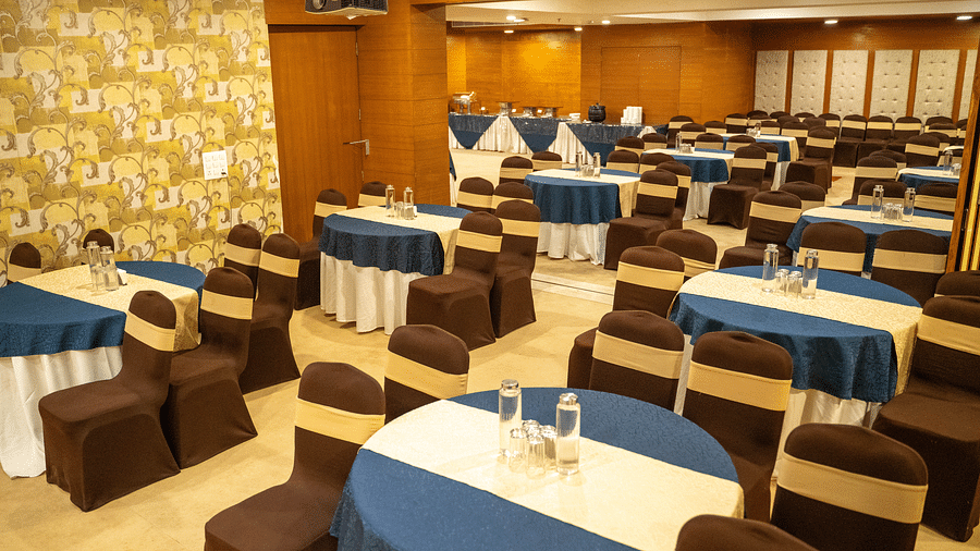 A well-lit event space with round tables, a wooden backdrop, and warm decor - Hotel Udai Median, Udaipur.