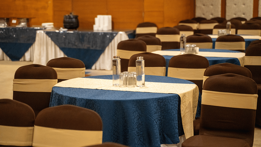 A banquet hall set up for an event, with neatly arranged round tables covered in blue tablecloths and brown chairs - Hotel Udai Median, Udaipur.