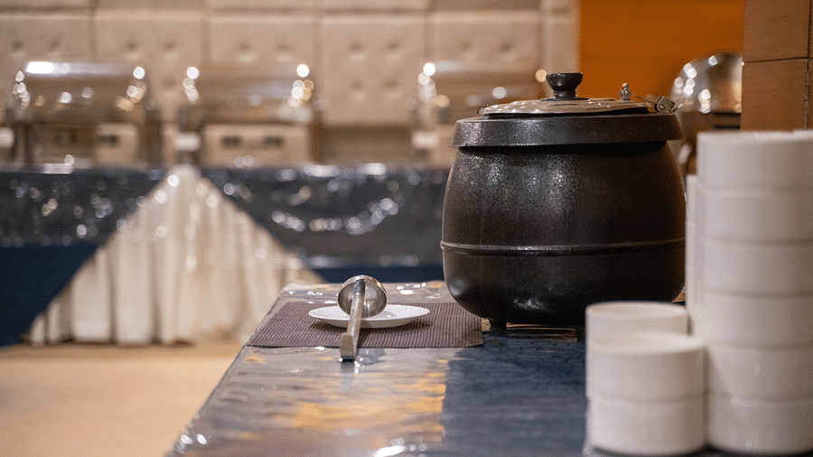 A buffet setup featuring a pot, stacked bowls, and cutlery on a polished counter - Hotel Udai Median, Udaipur.