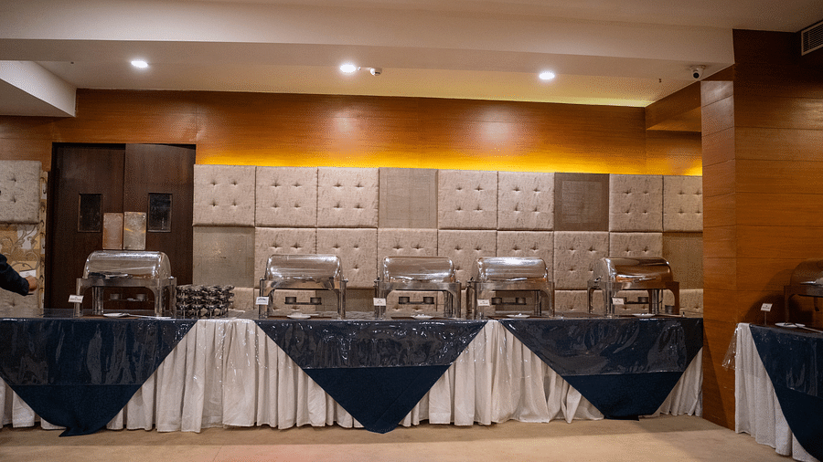 Image of a buffet table with chafing dishes, set against a wall with textured panels and warm lighting - Hotel Udai Median, Udaipur.