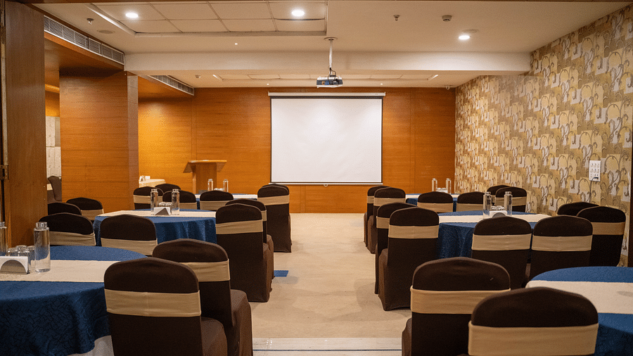 A well-lit conference room with round tables, brown and beige chairs, and a presentation screen - Hotel Udai Median, Udaipur.