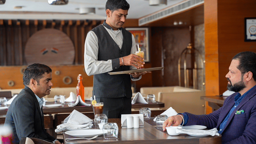 A hotel waiter taking an order from two people in a refined dining setting - Hotel Udai Median, Udaipur.