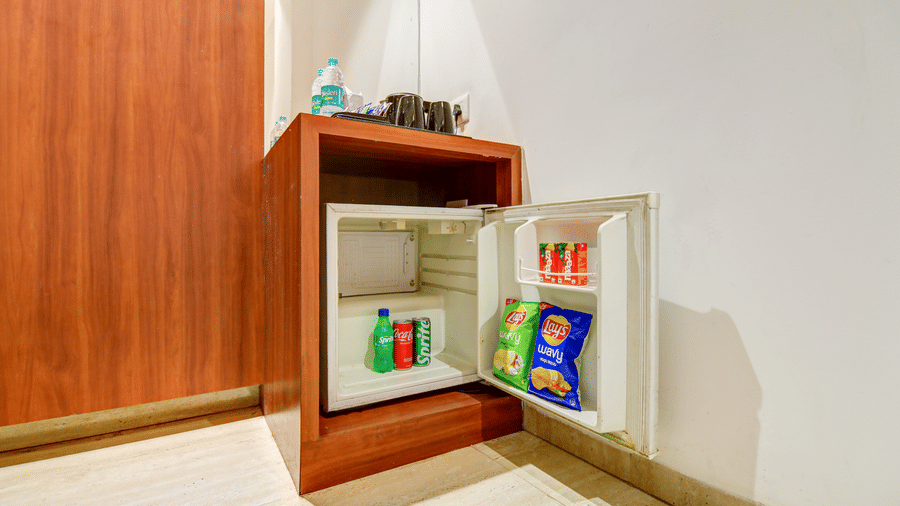 Open wooden cabinet revealing a mini-fridge stocked with drinks and snacks for guests - Hotel Velocity