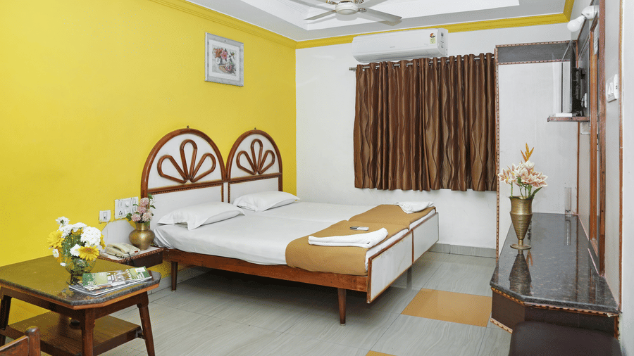 A double bedroom at Hotel Vikram with a large double bed with a wooden headboard, warm yellow interior lighting, and a seating area.